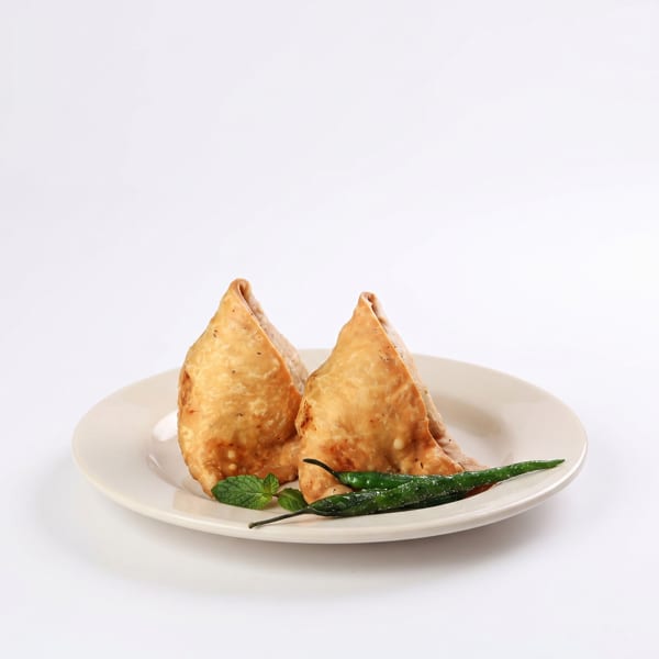 Two golden-brown samosas on a plate, garnished with green chilies and fresh mint leaves.